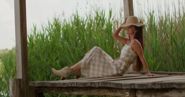 Rilassante giovane donna seduta sul molo di legno al lago calmo - Filmati, video