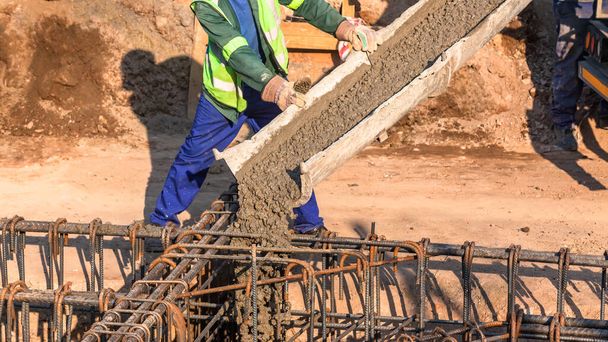 Baubeton, der von einem Zementwagen in Stahlfundamente gegossen wird, hautnah abstrakter Bauprozess vor Ort. - Foto, Bild