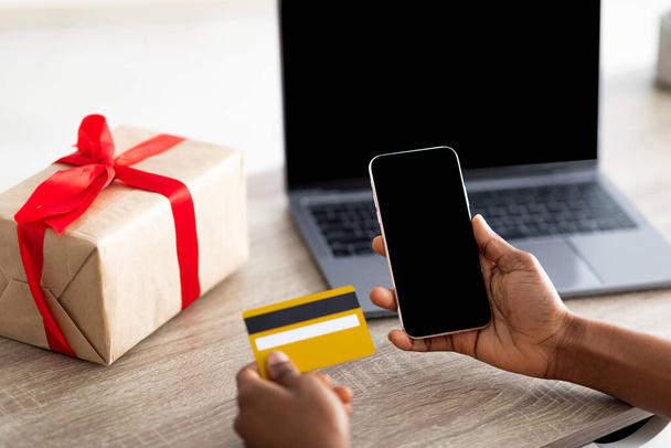 Крупним планом чорна жінка використовує сучасний смартфон, ноутбук і кредитну картку для покупки подарунків онлайн з дому, макет
 - Фото, зображення