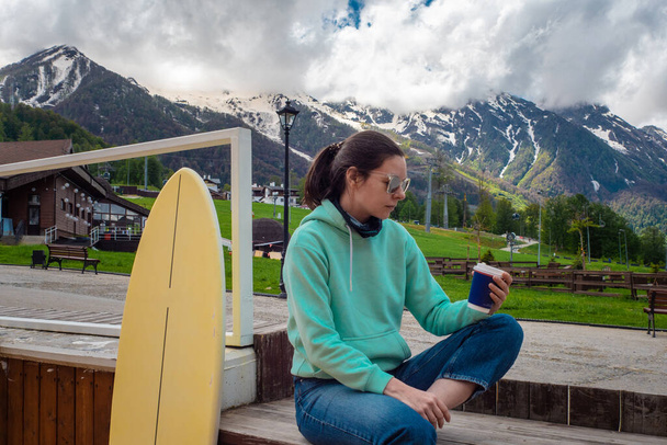 Local travel, a young woman in a blue hoodie is sitting in a cafe in a mountain village, - Foto, imagen