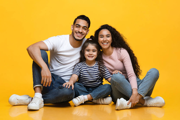 Portret van lachende Arabische ouders en kleine dochter poseren over gele achtergrond - Foto, afbeelding