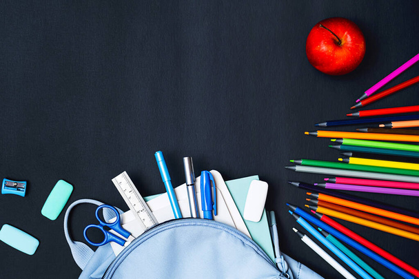 Okula dönelim. Sırt çantası, defterler, kalemler, renkli kalemler ve siyah masada elma. Çeşitli kırtasiyelerin düz uzantısı, boşluğu kopyala. - Fotoğraf, Görsel