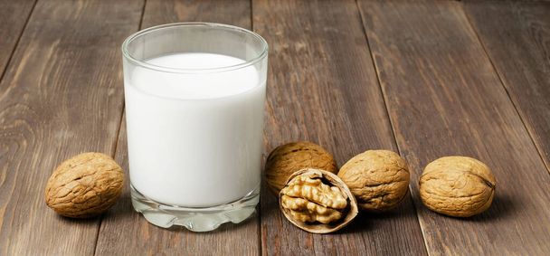 Milk from walnuts and nuts on a brown wooden background. Products containing vegetable protein, vitamins, and useful amino acids. - Zdjęcie, obraz