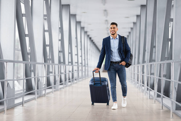Porträt eines jungen Mannes aus dem Nahen Osten, der mit Gepäck im Flughafenterminal spaziert - Foto, Bild