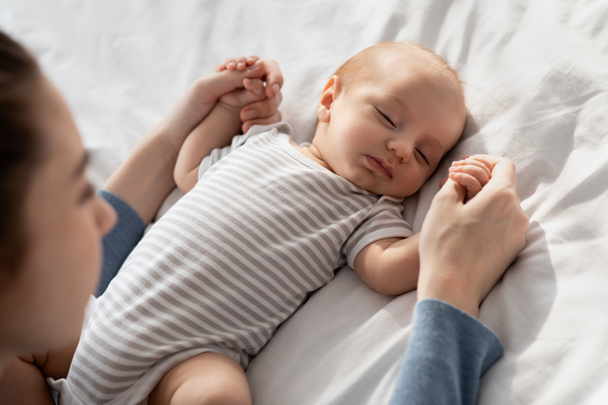 Soins maternels. Maman aimante tenant les mains de son adorable nouveau-né endormi - Photo, image