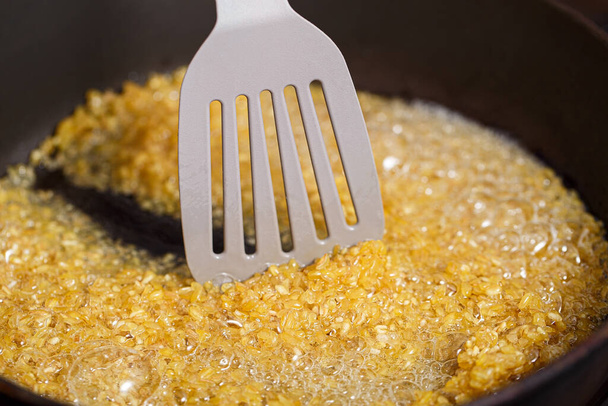 Bulgur frit dans une poêle. Grains de blé aromatisés au caramel mélangés à une spatule de cuisine à l'huile bouillante - Photo, image