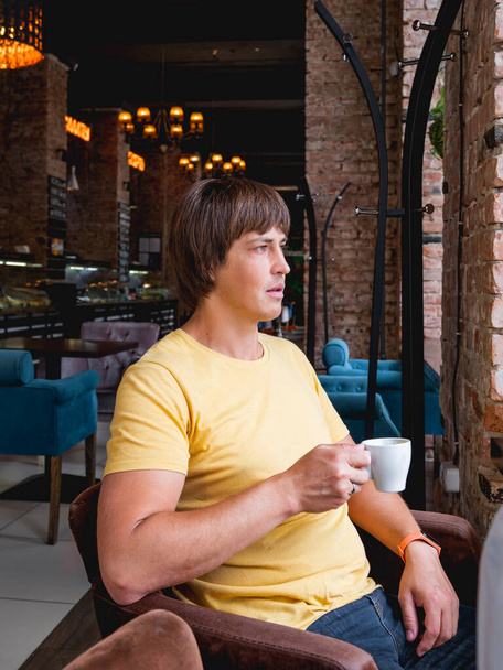Man drinks coffee in cafe. Loft designed interior with red brick walls and plush chairs. Breakfast and morning cup of coffee away from home. - Valokuva, kuva
