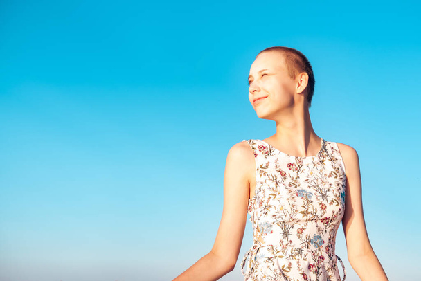 fille adolescente dans une robe avec une coupe de cheveux courte regardant au loin, plissant au soleil, sur le fond du ciel bleu - Photo, image
