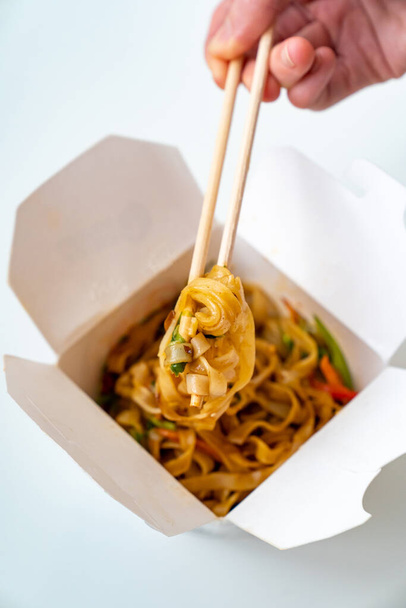 Παράδοση έτοιμων ασιατικών τροφίμων. noodles με λαχανικά και θαλασσινά σε λευκό κουτί και sushi sticks. Υπέροχο δείπνο. παραγγείλετε φαγητό από το τηλέφωνο ή online.  - Φωτογραφία, εικόνα