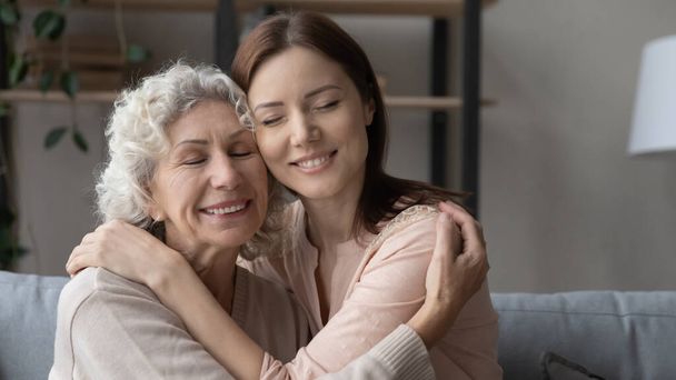 Elderly mother grown daughter hug with closed eyes touch heads - Foto, immagini