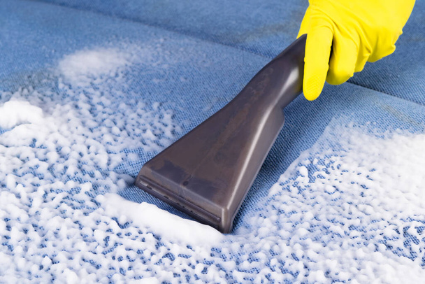 cleaning a blue upholstered sofa with special foam using a brush on a vacuum cleaner - Foto, Bild