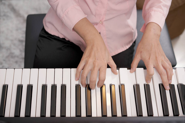 Ενηλίκων γυναίκα παίζει ηλεκτρονικό πιάνο με φύλλο σημείωμα. Newby πιανίστας εξάσκηση και εκμάθηση πώς να παίξει το τραγούδι. - Φωτογραφία, εικόνα