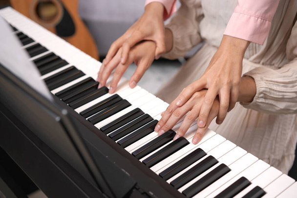 Duet adult women play electronic piano with note sheet. Newby pianist practicing and learning how to play song together as duo - Photo, Image