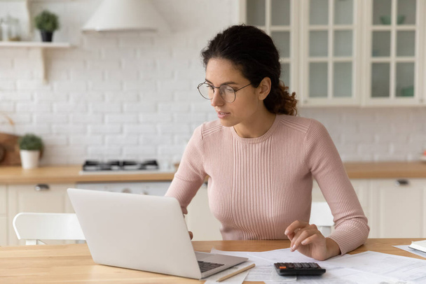 Focused millennial woman in eyeglasses paying bills online. - Fotó, kép