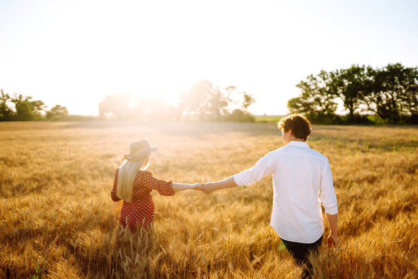 Young happy couple hugging on  a wheat field, on the sunset. Enjoying time together. The concept of youth, love and lifestyle. - Fotoğraf, Görsel