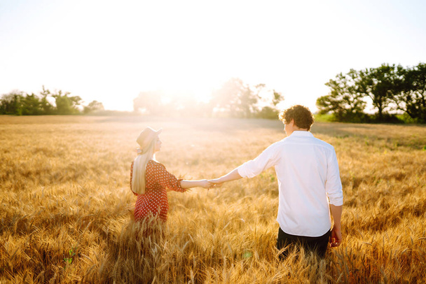 Young happy couple hugging on  a wheat field, on the sunset. Enjoying time together. The concept of youth, love and lifestyle. - Fotografie, Obrázek