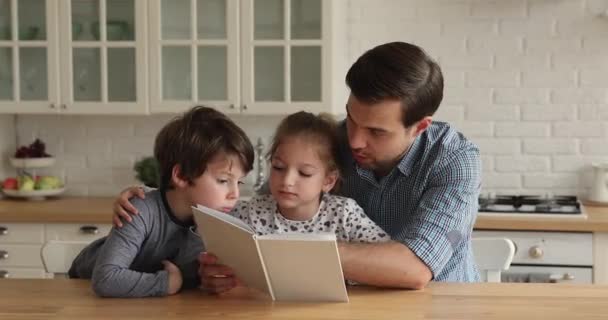 Pečující mladý tatínek učí číst malé děti doma. - Záběry, video