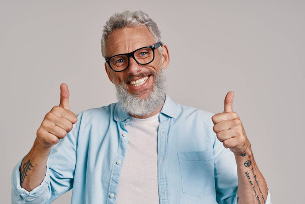 Handsome senior man in eyeglasses keeping thumbs up and smiling - Foto, immagini