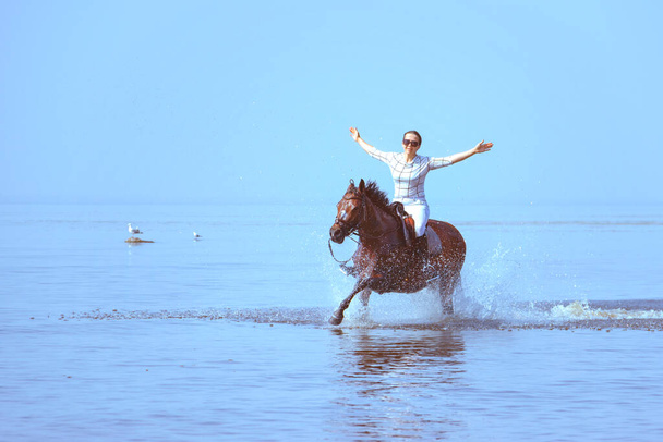 Young woman rides a horse on the water with her arms outstretched - 写真・画像
