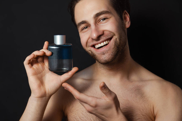 Shirtless white man smiling while showing cologne isolated over blue wall - Fotoğraf, Görsel