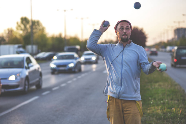 Liikenteessä toimiva jonglööri. Juggler mies esiintyy liikennevaloissa, esityksen jälkeen hän pyytää kuljettajia lahjoituksen. - Valokuva, kuva