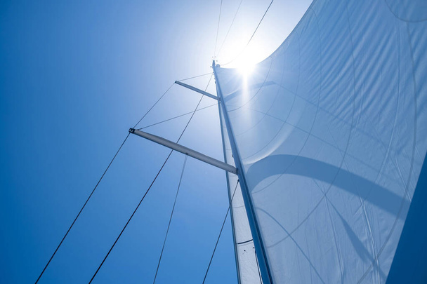 オープン海での風とセーリング、夏休みのコンセプト。ヨットの風が澄んだ青空の背景に帆を記入。空を見上げ、太陽が輝き、ボートのリギングで日光を浴び、低角度のビュー - 写真・画像