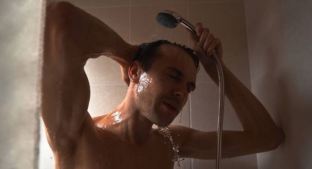 Portrait of young handsome man washes himself with shower gel, lathers head with shampoo in the bathroom at home close-up - Fotografie, Obrázek
