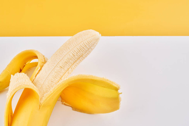 Plátano medio pelado sobre fondo blanco amarillo con espacio para copiar - Foto, Imagen