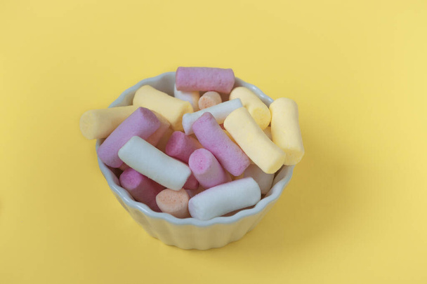 Multicolored marshmallows in a bowl on a yellow background. Mockup of packaging, postcard or card, close-up top view - Valokuva, kuva