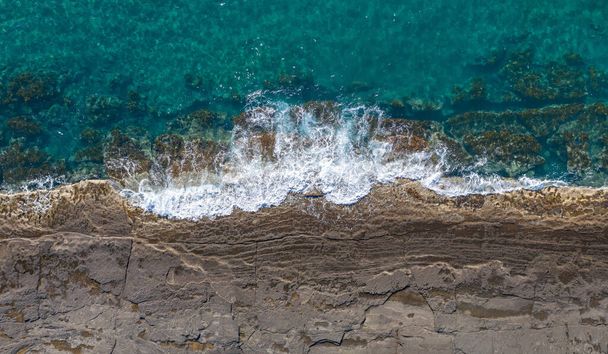 キプロスのポモス近くで波が壊れ岩の海岸線の空中パノラマ - 写真・画像