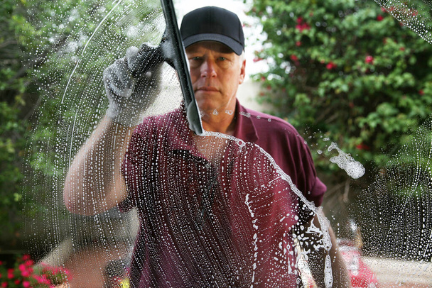 Raam wassen. Raamreiniging. Raamreiniger. Schoonmaken van ramen. een professionele glazenwasser zeept en knijpt een raam schoon. Raamreiniger met behulp van een trekker om een raam te wassen. Een man die een raam schoonmaakt. Professionele raamreiniging. - Foto, afbeelding