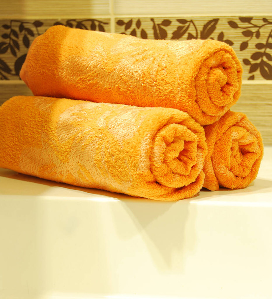 Drei orange Handtücher auf einem keramischen Waschbecken in einem luxuriösen und sauberen Badezimmer - Foto, Bild