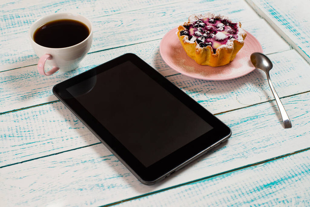 A digital tablet, a cup of coffee and a cake basket with berries and cottage cheese on a white and blue vintage table. Morning breakfast background. - Foto, Bild