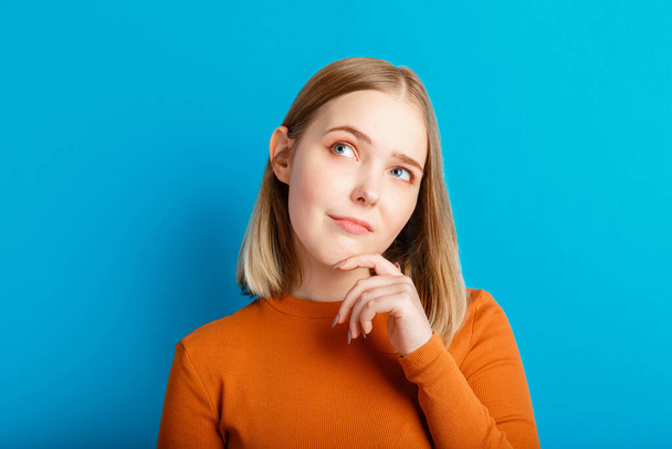 Young woman think thought. Portrait of emotional teenager girl looking on empty space deep thinking about idea or question isolated on color blue background with copy space. - Valokuva, kuva