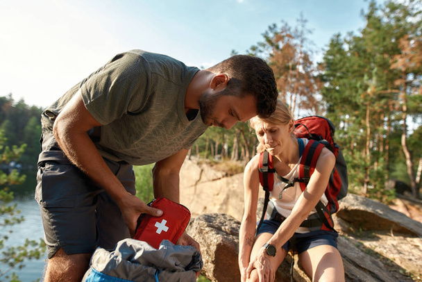 Young man using first aid kit on injured leg - Фото, изображение