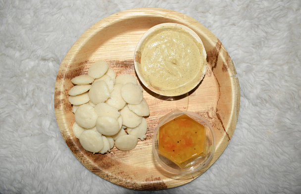 Delicious Mini button idli with hot Sambar and mungfali peanut chutney served in eco friendly bio disposable plates and bowls.South Indian breakfast item dish.Idlis prepared with flattened rice batter - Photo, Image