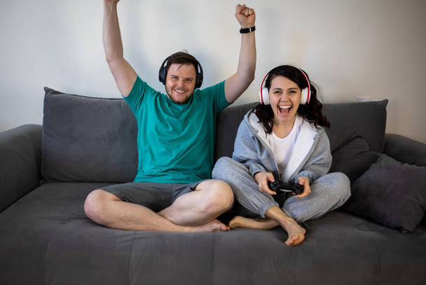 ζευγάρι που παίζει βιντεοπαιχνίδια μαζί κάθεται στον καναπέ - Φωτογραφία, εικόνα