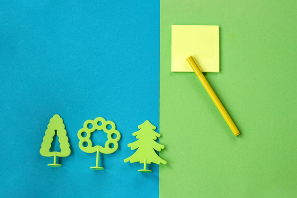 Minimum set of school and office supplies on bright turquoise and green background: pen, note paper and toy trees. Concept: back to school. Flatlay, top view. - Fotó, kép