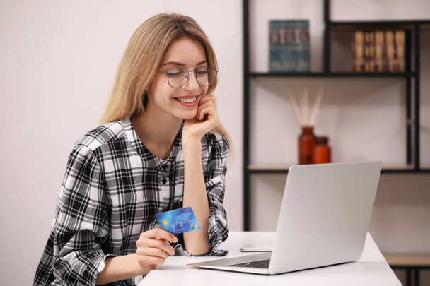 Frau mit Kreditkarte nutzt Laptop für Online-Einkäufe an weißem Tisch - Foto, Bild