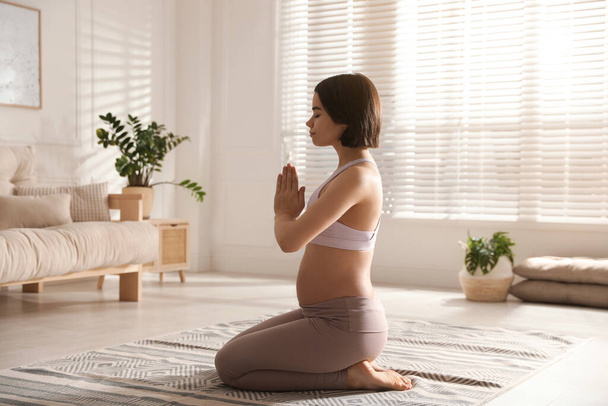 Young pregnant woman practicing yoga at home - Фото, изображение