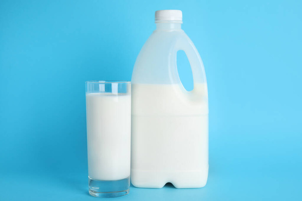Gallon bottle and glass of milk on light blue background - Фото, изображение