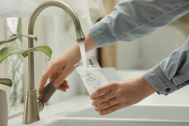 Woman filling glass with water from tap at home, closeup - Foto, imagen