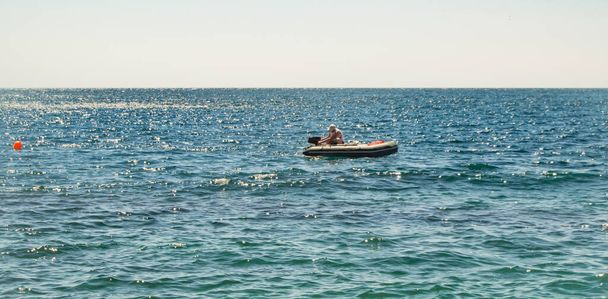 Un barco de goma defectuoso con un motor, un hombre enciende el motor, un día de verano en un mar tranquilo. - Foto, imagen