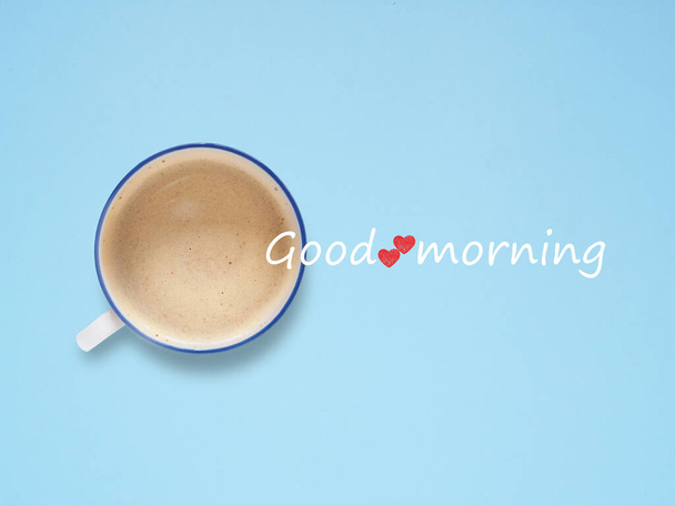The word "Good morning" with small red heart on coffee cup over blue background. Top view, flat lay, space for text - Foto, Imagem
