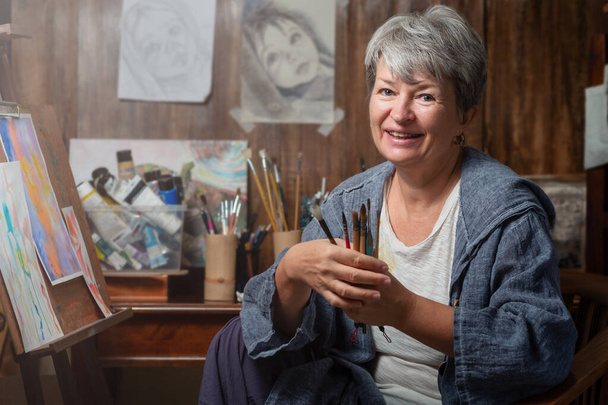 Портрет художника с кисточками и картинами. Женщина занимается своим хобби - Фото, изображение