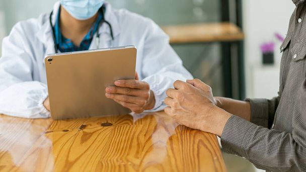 Ein Arzt berät einen Patienten im Büro mit einem Arzt, der ein Tablet in der Hand hält - Foto, Bild