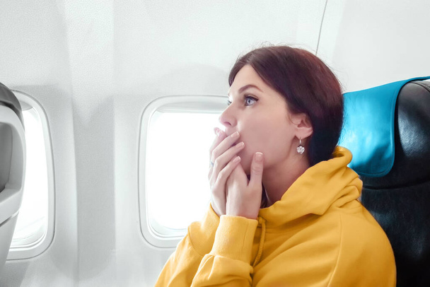 The girl flies on the plane, frightened closed his mouth with his hands, so as not to shout. Concept by follow. Flying by plane - Foto, afbeelding