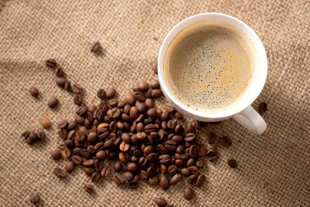 Kopje koffie met gebrande koffiebonen op bruine doek. - Foto, afbeelding