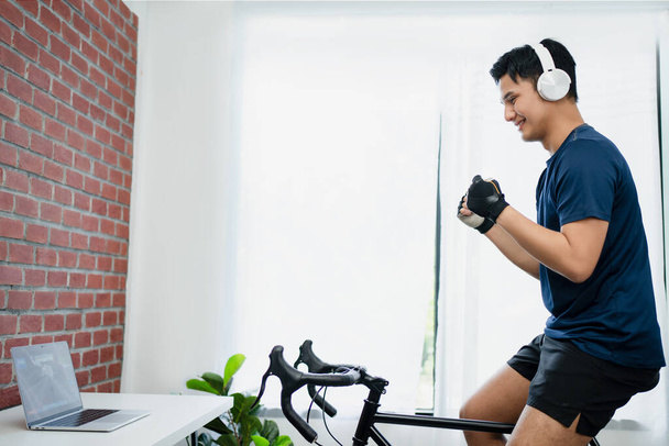 Asiatische Mann genießt Radfahren auf einem Trainer zu Hause in der Früh. - Foto, Bild