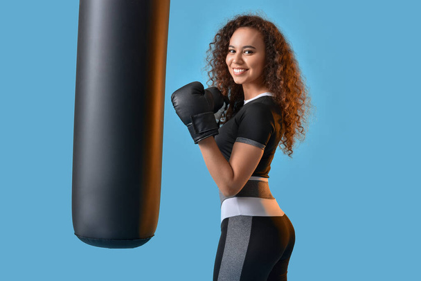 Kaunis nuori nainen nyrkkeilyhanskat nyrkkeilysäkki värillinen tausta - Valokuva, kuva